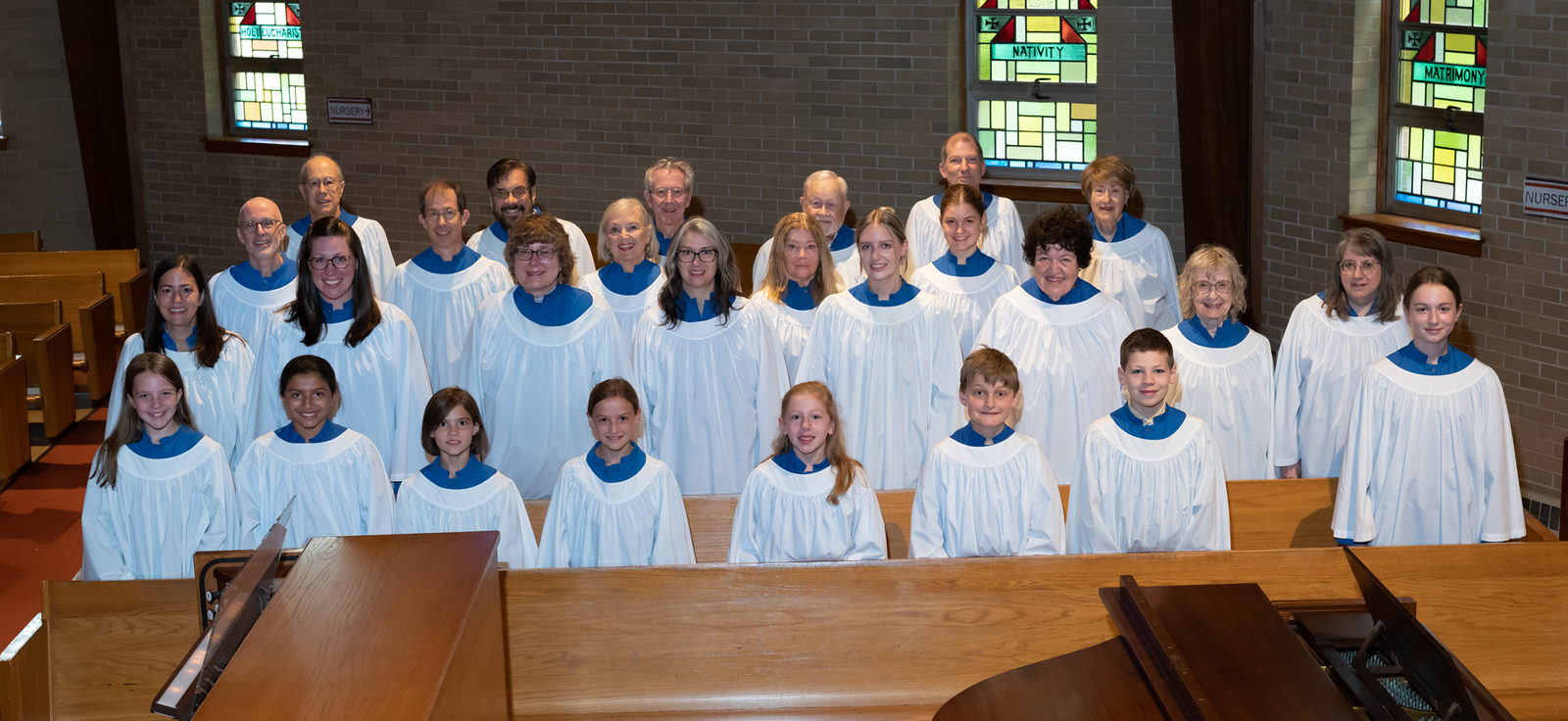 The choir stands in rows wearing white robes.